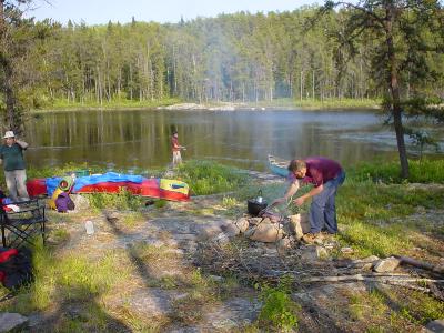 Al Bayne swatting bugs, Mike Brown preparing supper at our first campsite, while Travis in the background fishes