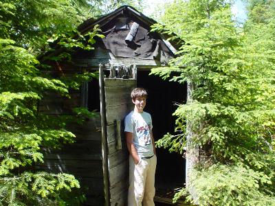 Travis standing in doorway of trappers cabin near the end of the portage